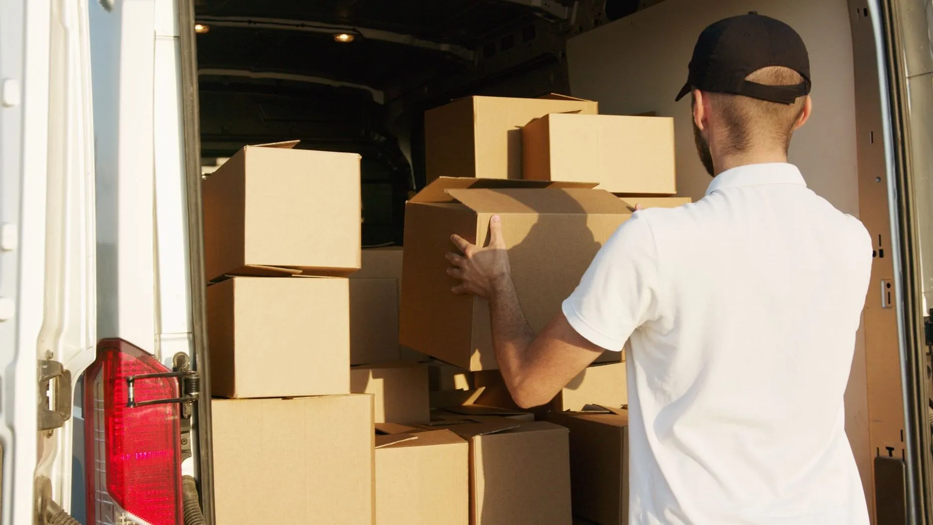 A mover in a white polo shirt loading plain cardboard boxes into the back of a van