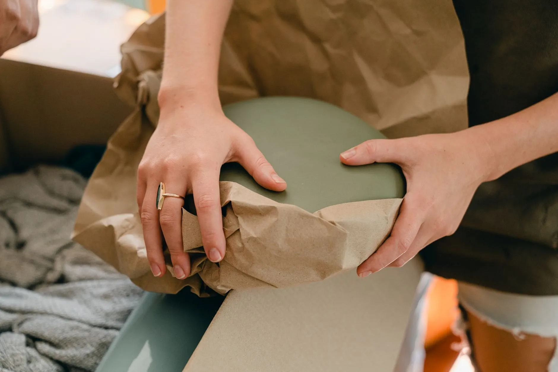 Hands wrapping a plate in brown packing paper over an open box